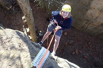 Woman wearing a yellow helmet repels down a rock while holding a rope